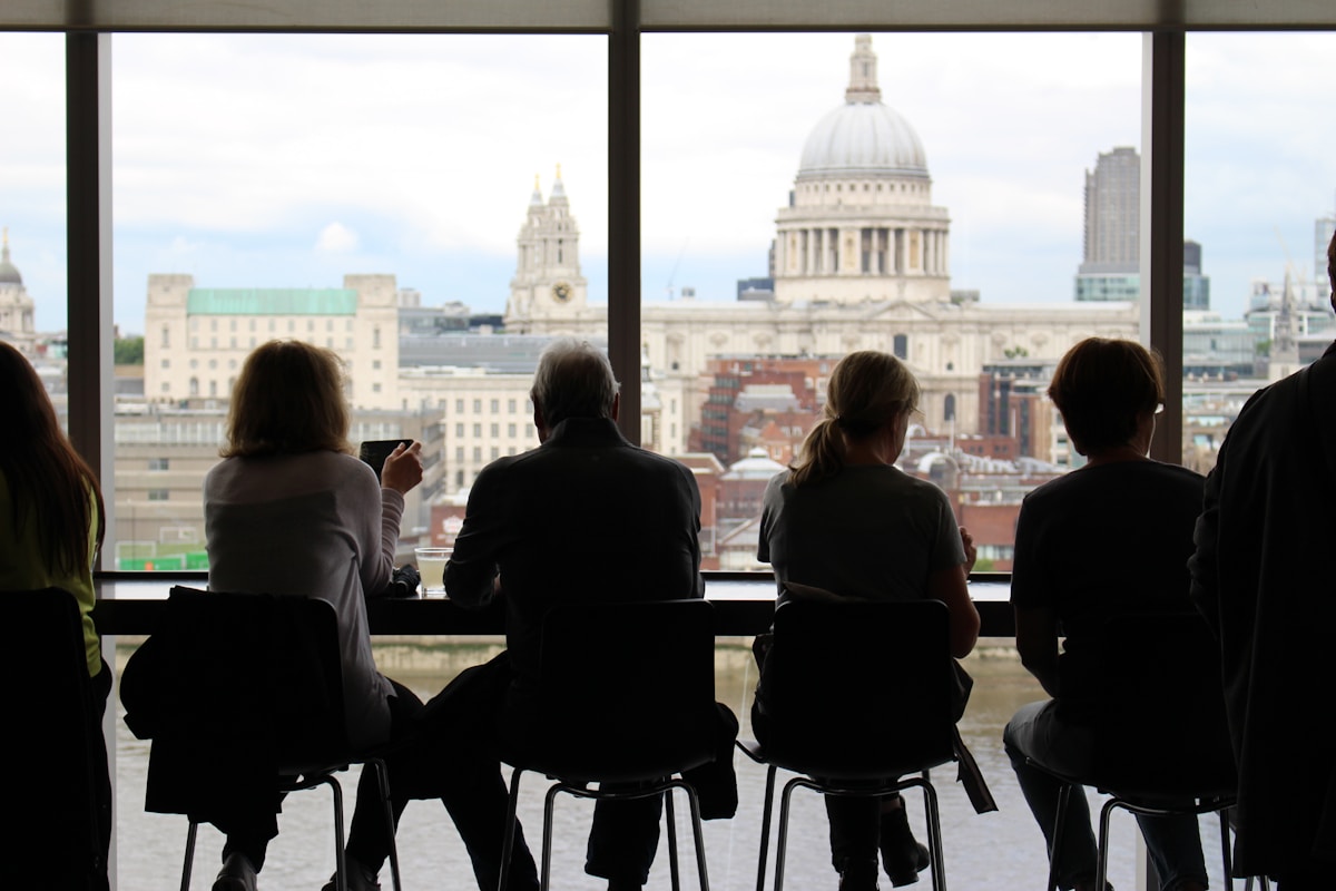 man in between of four women sits while watching on window - trip to London