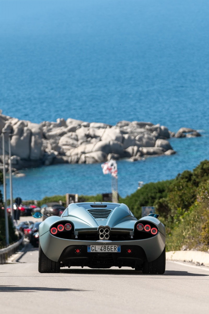 a blue sports car driving down a road next to the ocean - Sardinia Italy Travel Guide