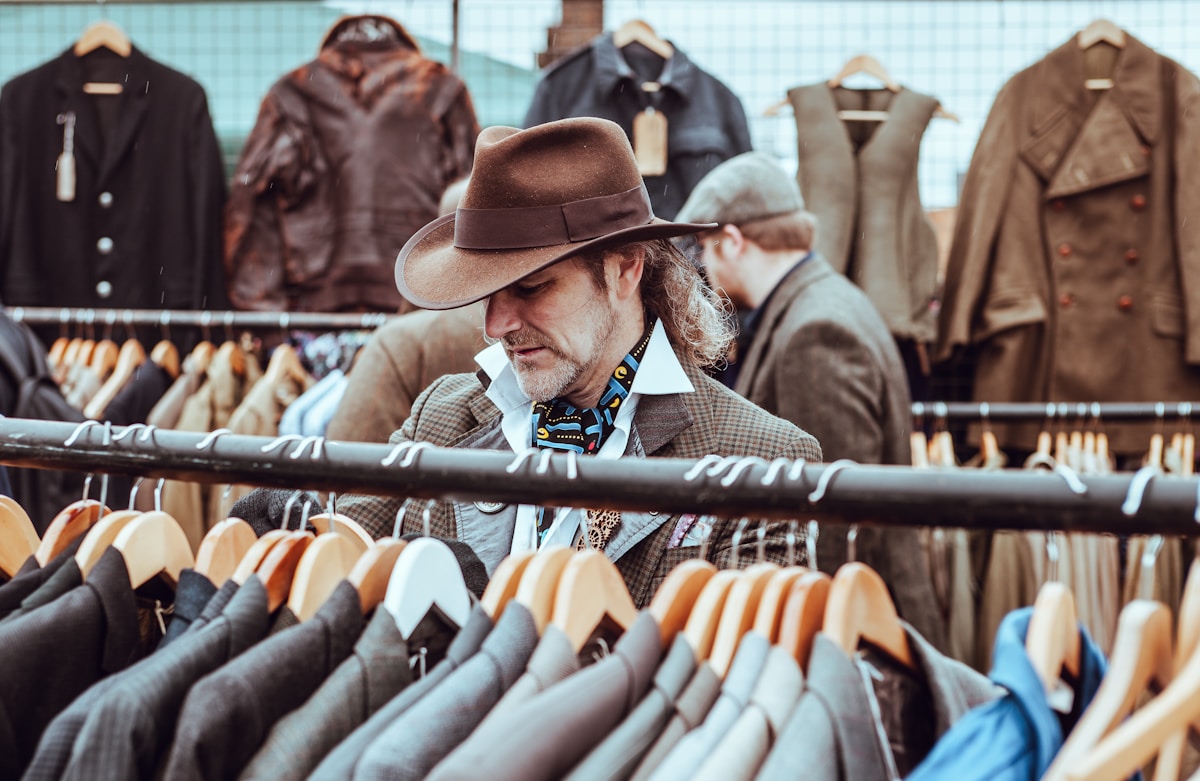 man in brown cowboy hat in front of hanged suit jackets - London Shopping