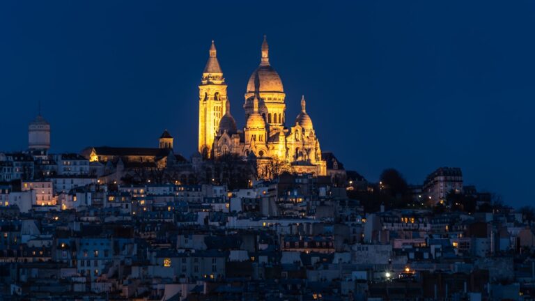 a very tall cathedral towering over a city at night - Basilica of the Sacred Heart of Paris