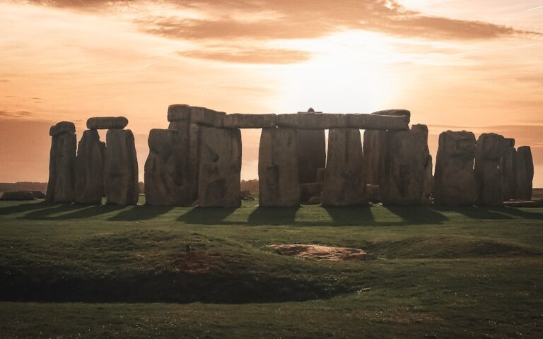 a stonehenge in a field with the sun setting behind it - Day trips from London England