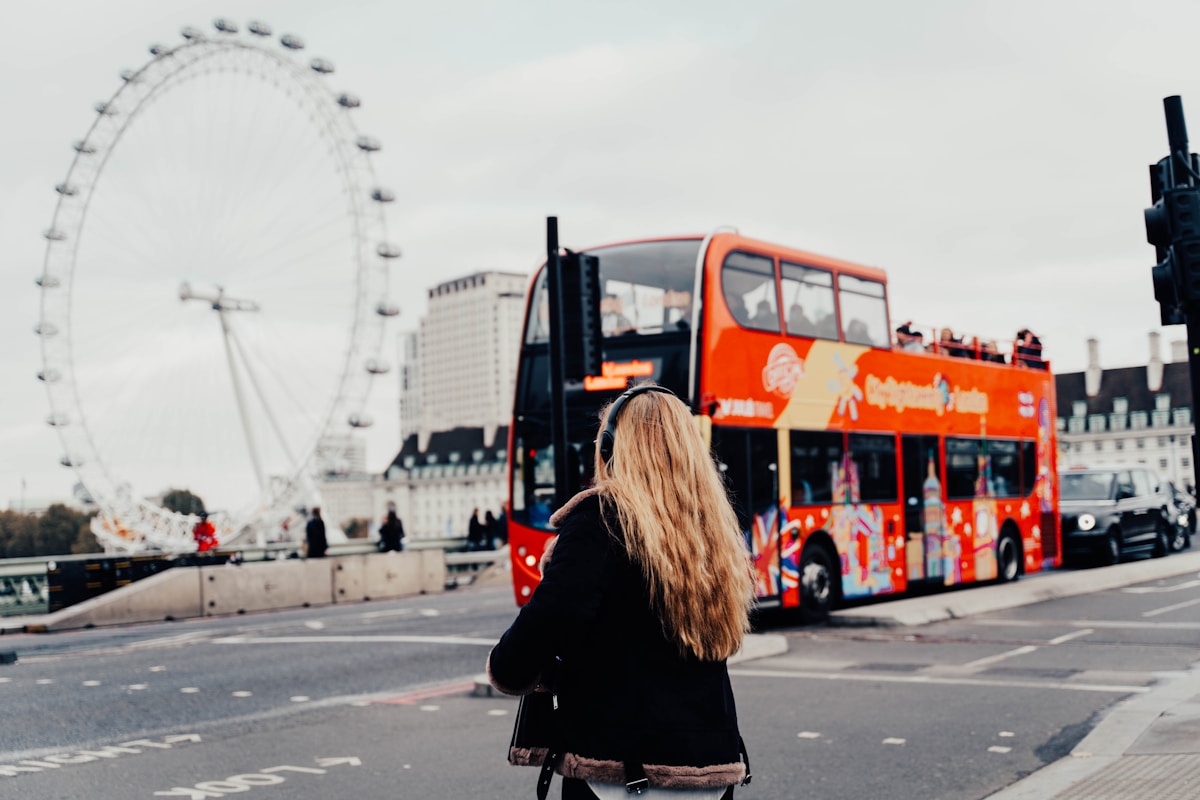 a woman standing in front of a red double decker bus - London Transportation, visiting London for the first time