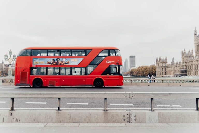 a red double decker bus driving down a street - London Transportation