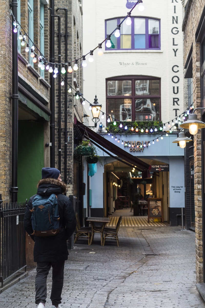 person wearing blue backpack while walking on narrow street - where to stay in London