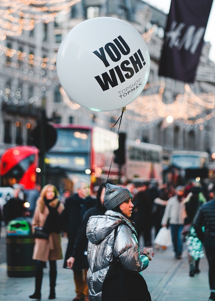 woman walking on street with people holding balloon at daytime - Shopping in London