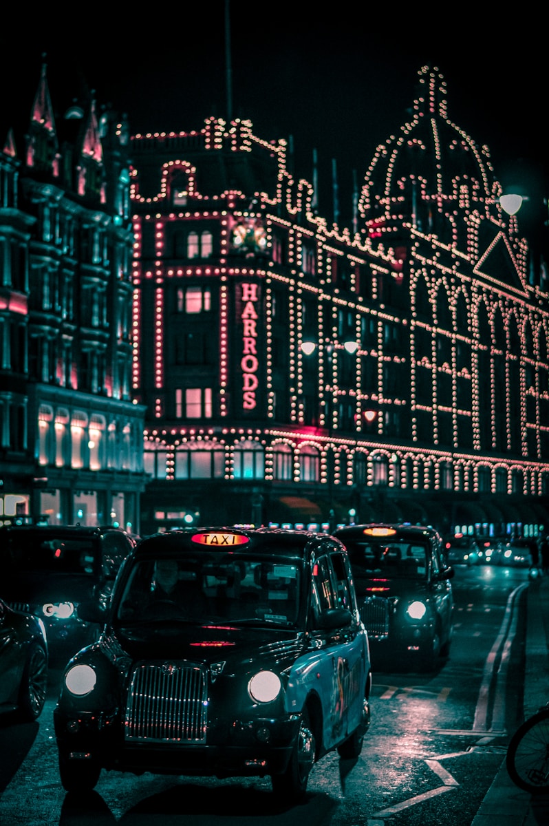 black taxi in the street passing trough Harrods Mall during nighttime - London Transportation