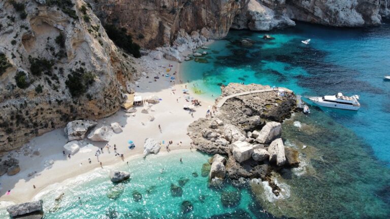 a group of people on a beach next to a body of water - Sardinia Travel Guide Italy