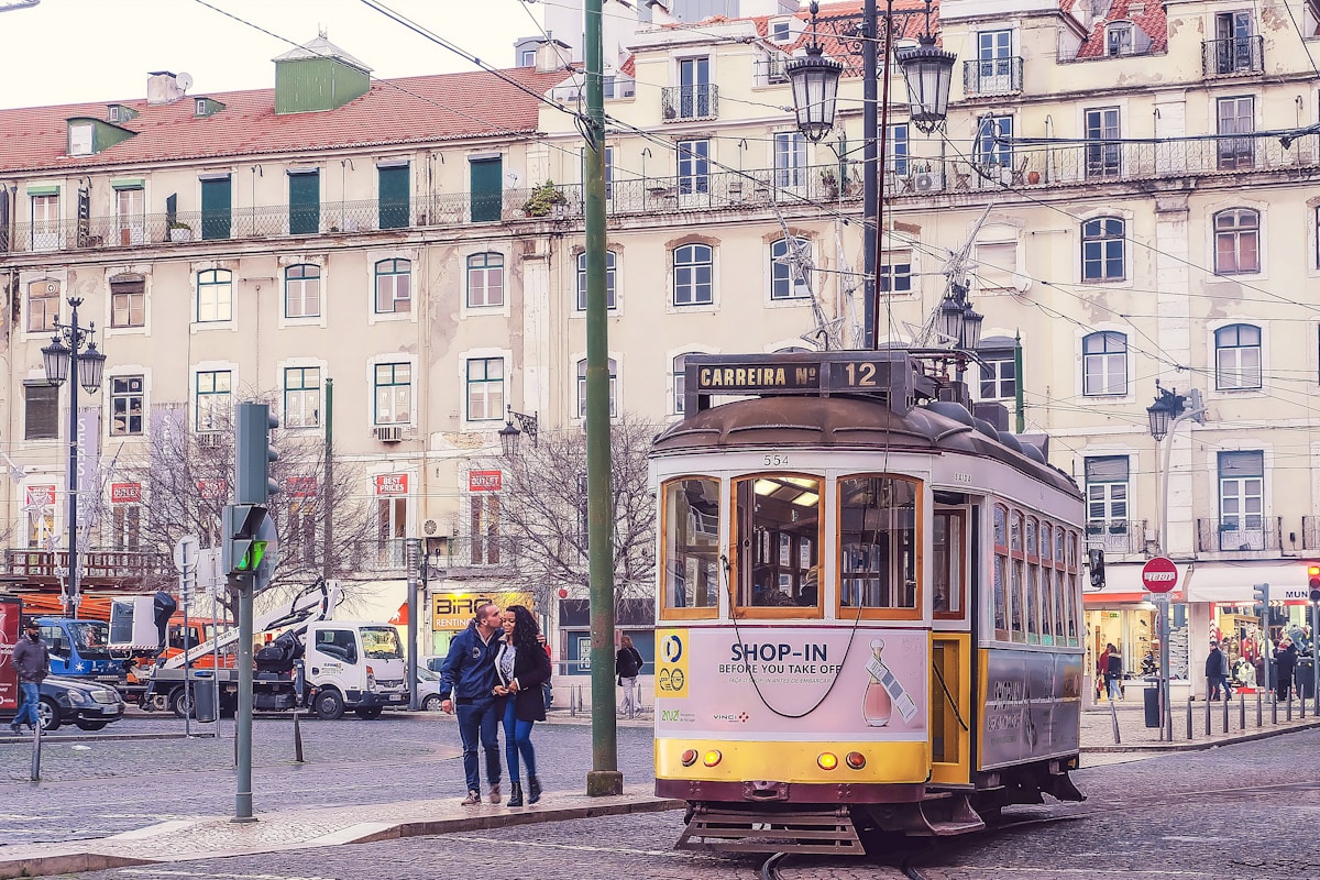 a couple of people standing on a street next to a trolley - Lisbon Transportation