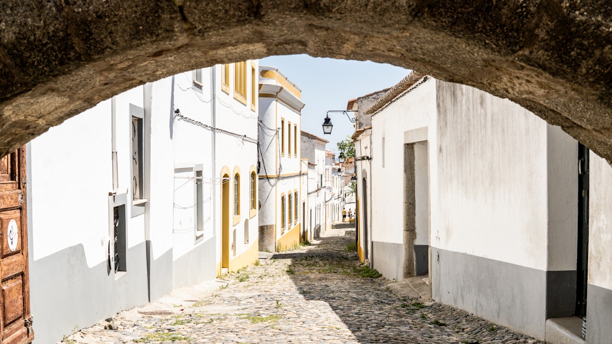 a narrow cobblestone street with white buildings - Évora Streets, Lisbon, Portugal