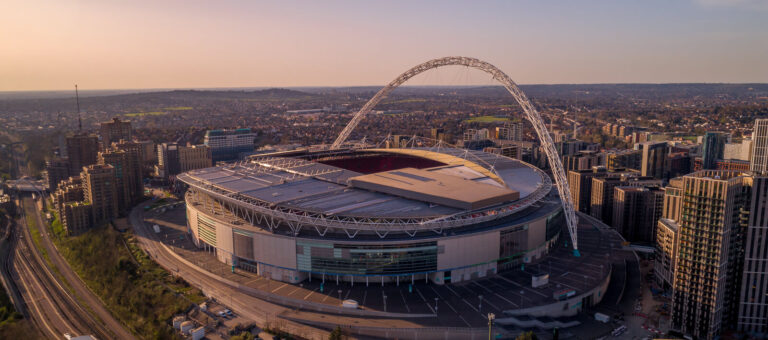 Wembley Stadium stands proudly against a sunset backdrop, showcasing its iconic arch and hosting major sporting events.