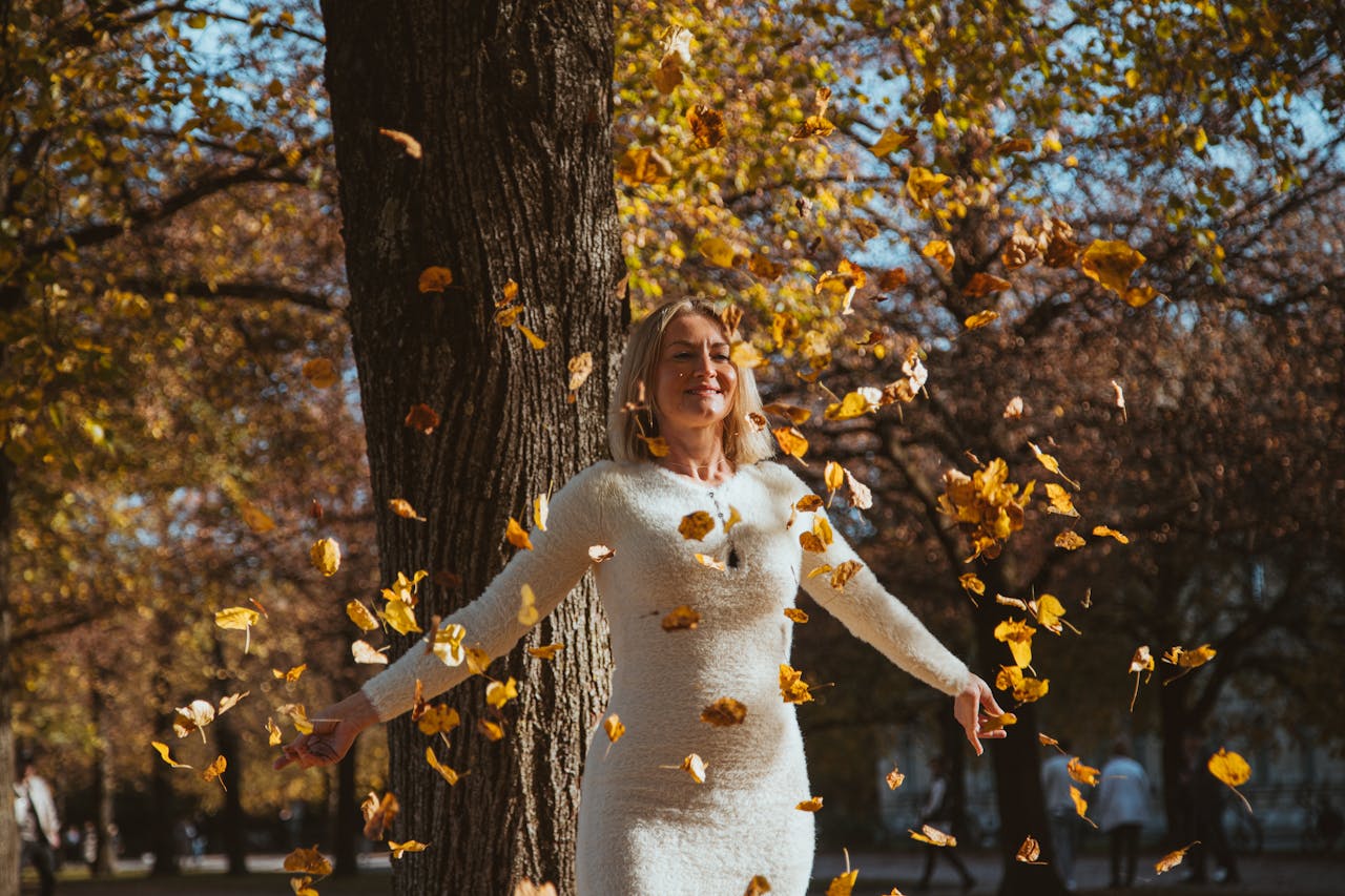 Best Time to Visit Munich, A woman in a white dress enjoying falling autumn leaves in an outdoor park in Munich, Germany.