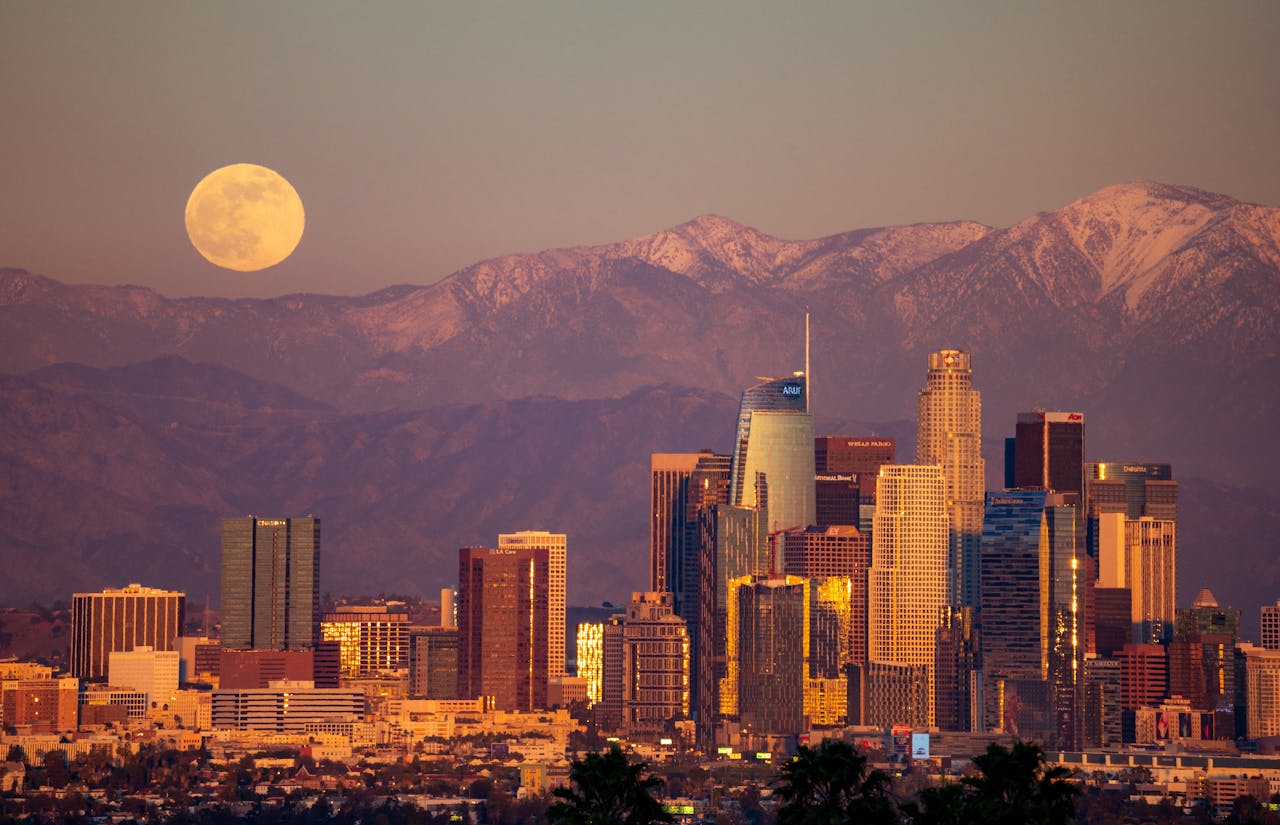 Captivating view of Los Angeles skyline with full moon and snow-capped mountains in the background.