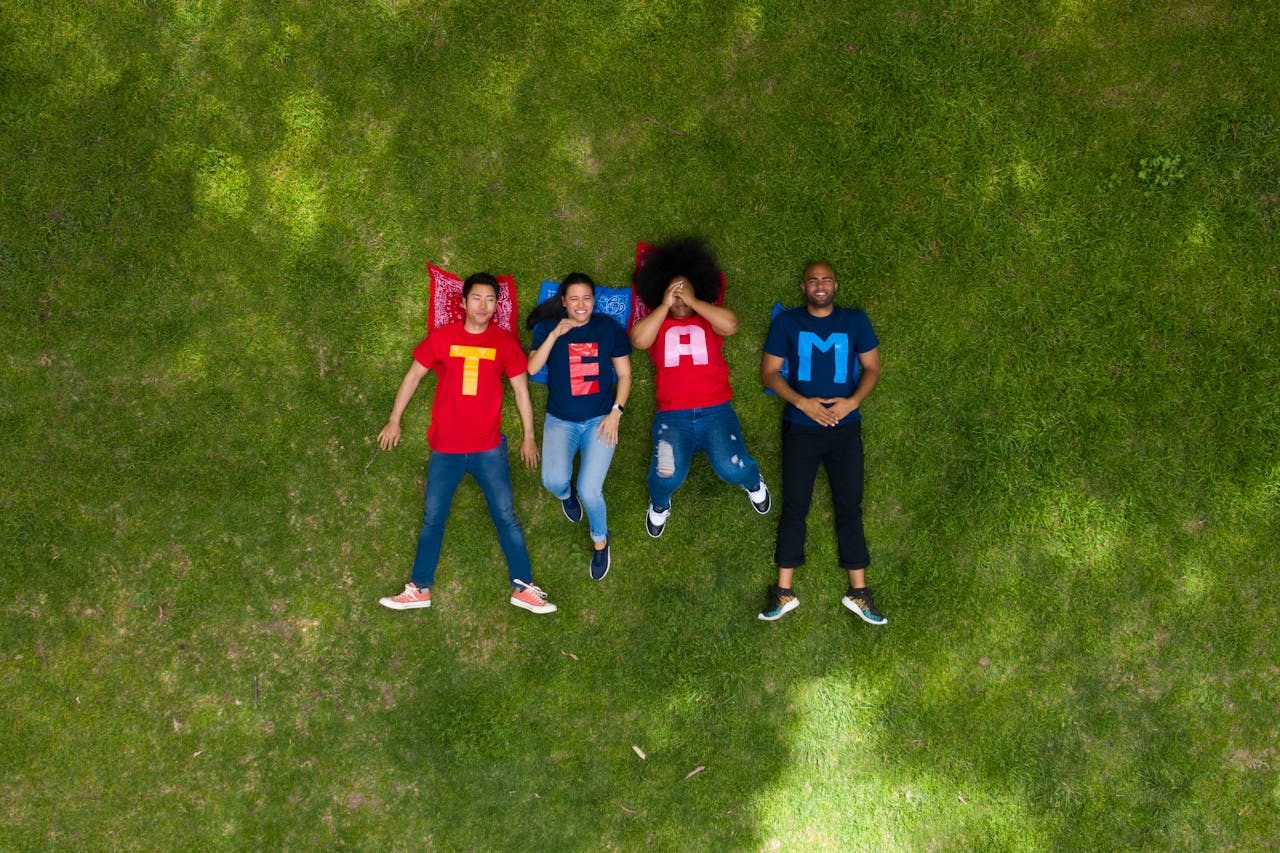 Diverse group of adults lying on grass with TEAM shirts, symbolizing teamwork and togetherness.