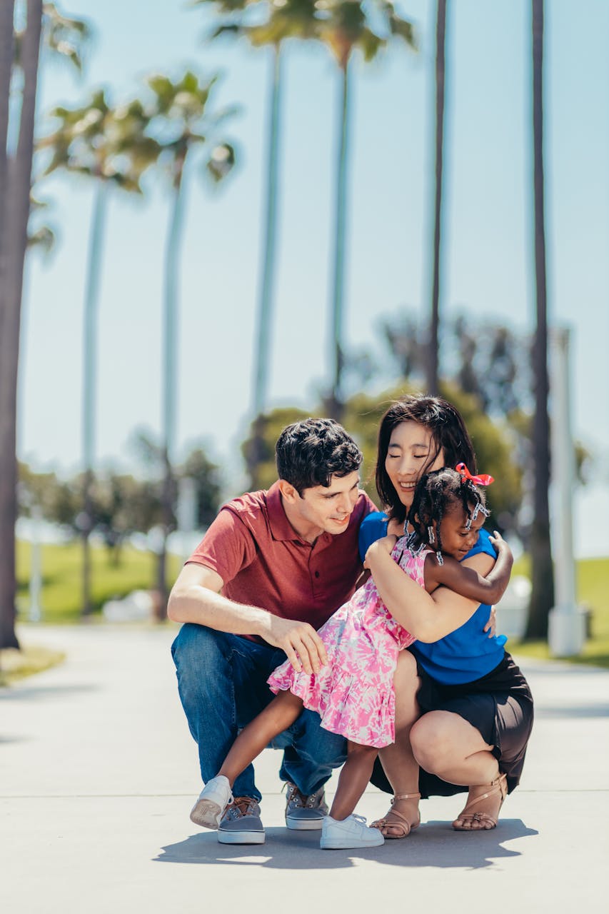 A joyful family enjoys bonding time outdoors, captured in a heartwarming hug against a palm tree background.
