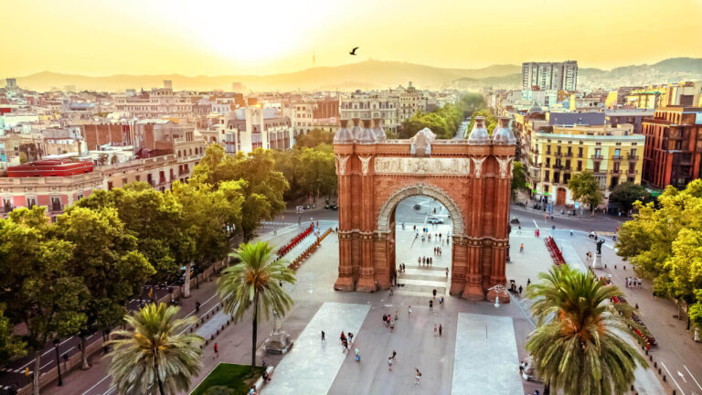 Sunset view of the Arc de Triomf in Barcelona, surrounded by vibrant streets and lush trees, embodying the city's charm.