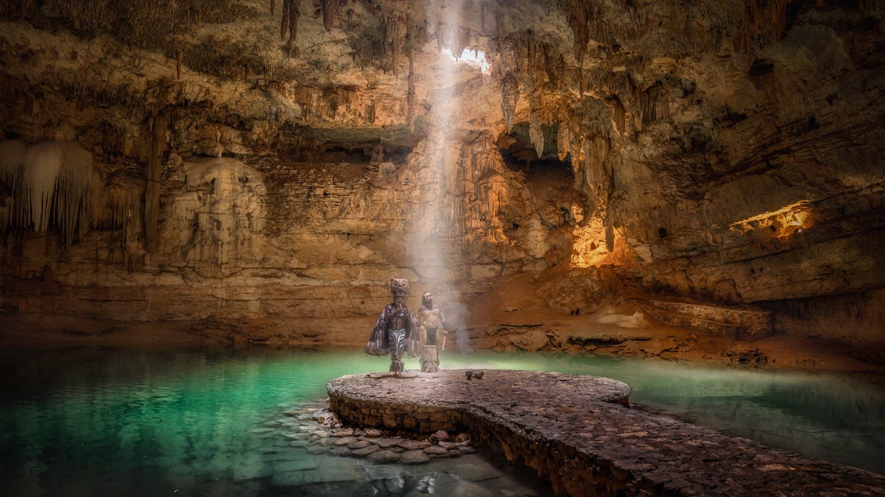 Stunning underground grotto with shimmering turquoise water and ethereal light highlighting ancient sculptures and formations.