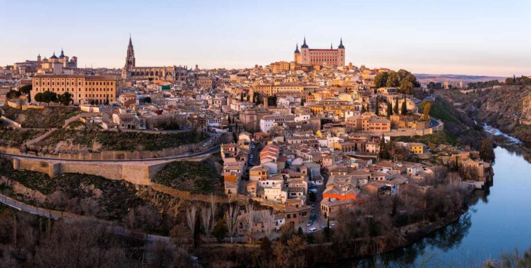 Historical skyline of Toledo, Spain, featuring medieval architecture and scenic landscape along the Tagus River at sunset.