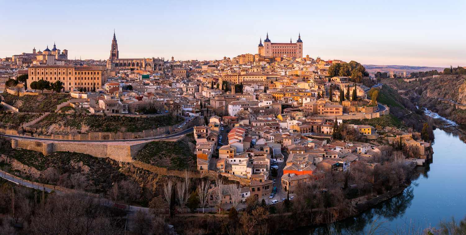 Historical skyline of Toledo, Spain, featuring medieval architecture and scenic landscape along the Tagus River at sunset.