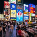 Bustling street in Osaka illuminated by vibrant neon signs, showcasing the city’s lively nightlife and cultural allure.