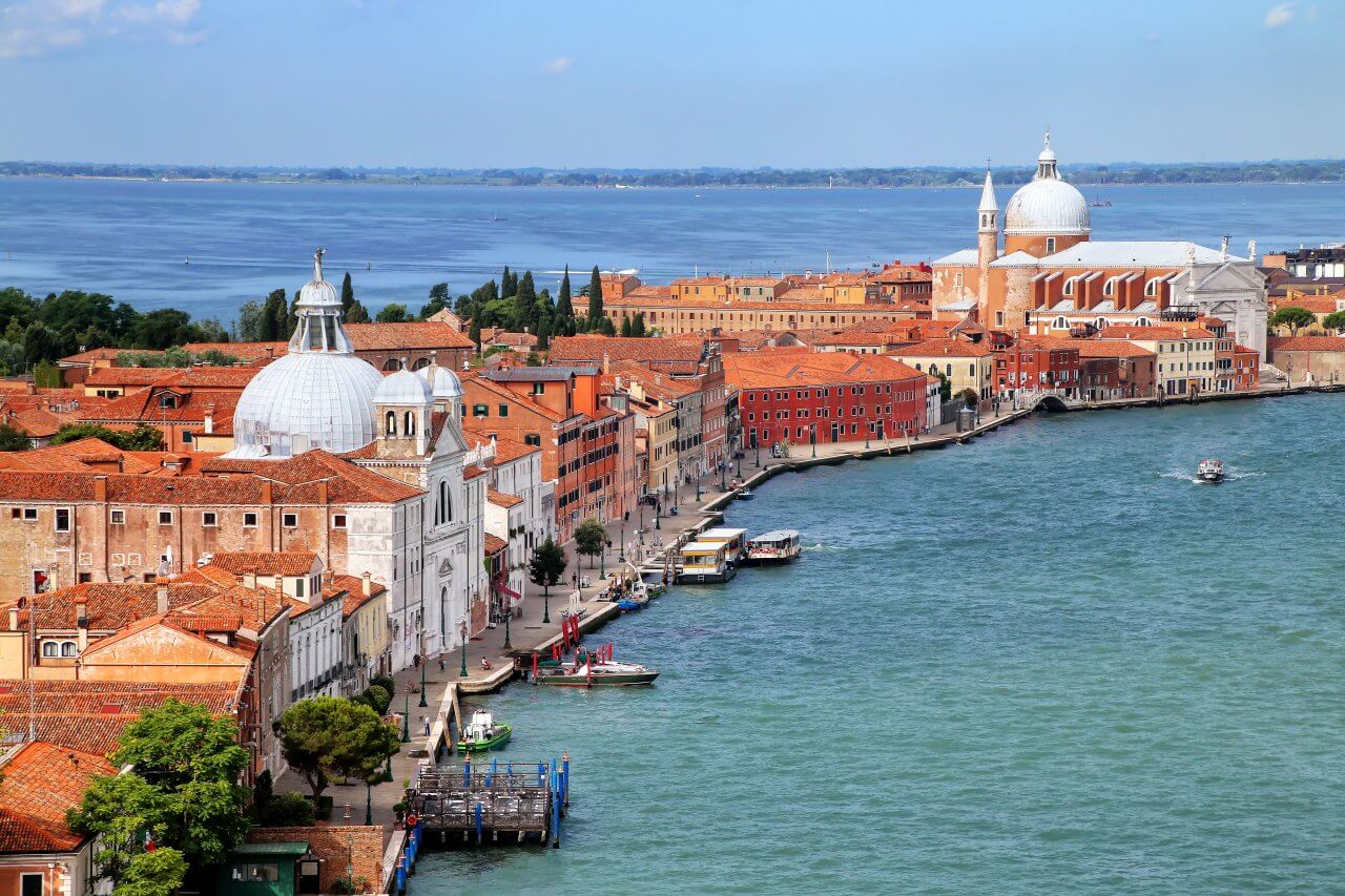 Scenic view of Venice showcasing vibrant buildings along the waterfront, with boats sailing on the shimmering lagoon.