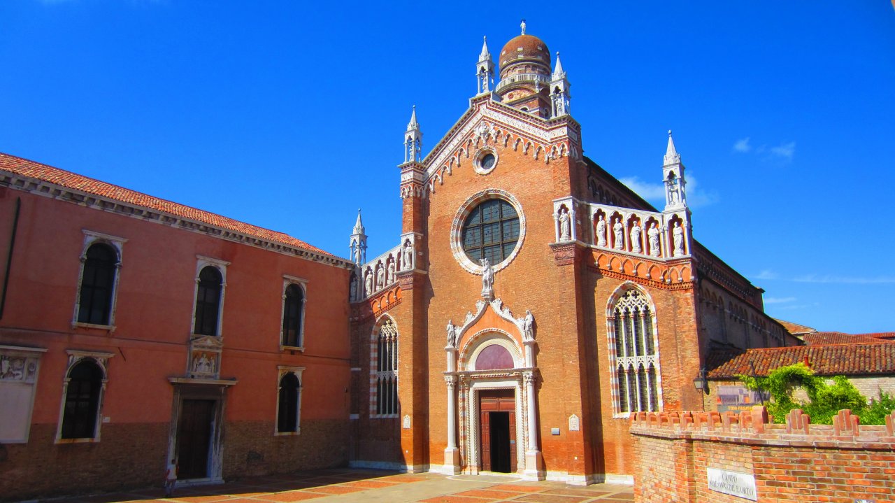 Historic brick Madonna dell'Orto church in Venice showcasing intricate architectural details against a clear blue sky, inviting exploration.