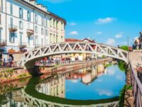 Charming canal scene in Milan featuring a unique bridge, bustling shops, and vibrant reflections by the water's edge.