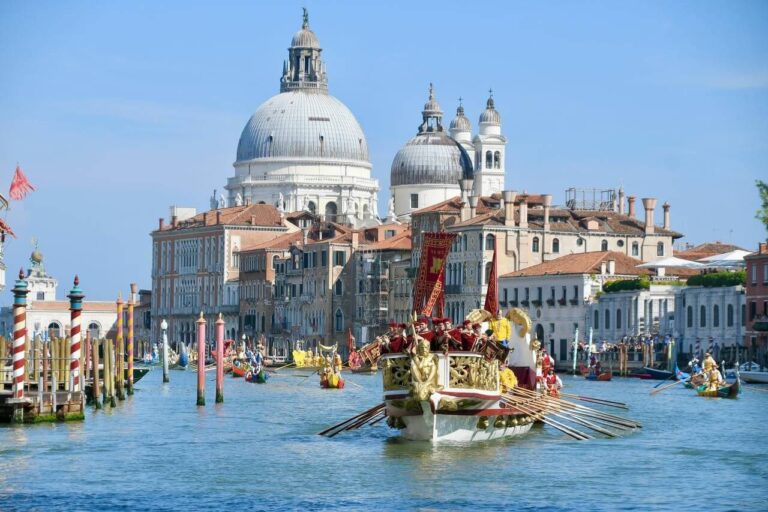 Venetian regatta on the Grand Canal, showcasing ornate boats and historic architecture under a bright blue sky.