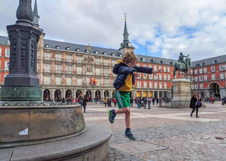Boy joyfully jumping in Madrid's Plaza Mayor, showcasing playful energy and the vibrant atmosphere of the historic square.