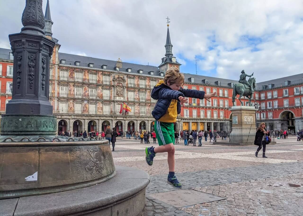 Boy joyfully jumping in Madrid's Plaza Mayor, showcasing playful energy and the vibrant atmosphere of the historic square.