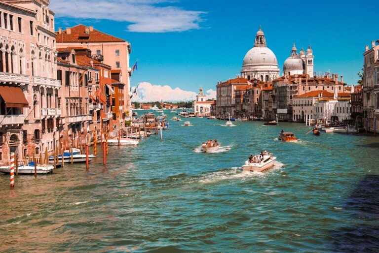 Gondolas and boats navigate the vibrant canals of Venice, showcasing stunning architecture under a bright blue sky.
