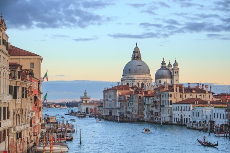 Venetian canal showcasing historic buildings with domes against a sunset sky, highlighting the city's enchanting charm.