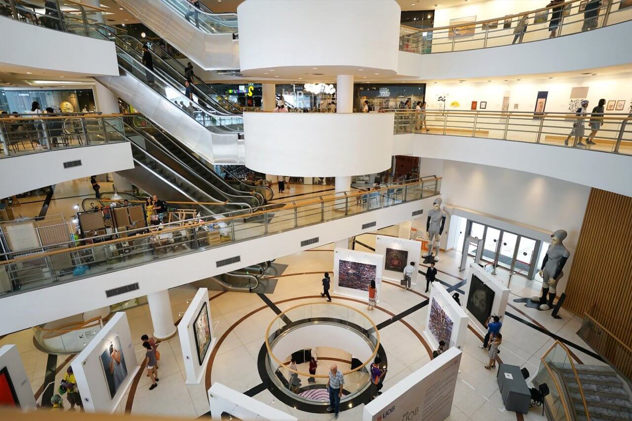 Modern shopping mall interior featuring art exhibitions, escalators, and visitors engaging in the vibrant cultural space.