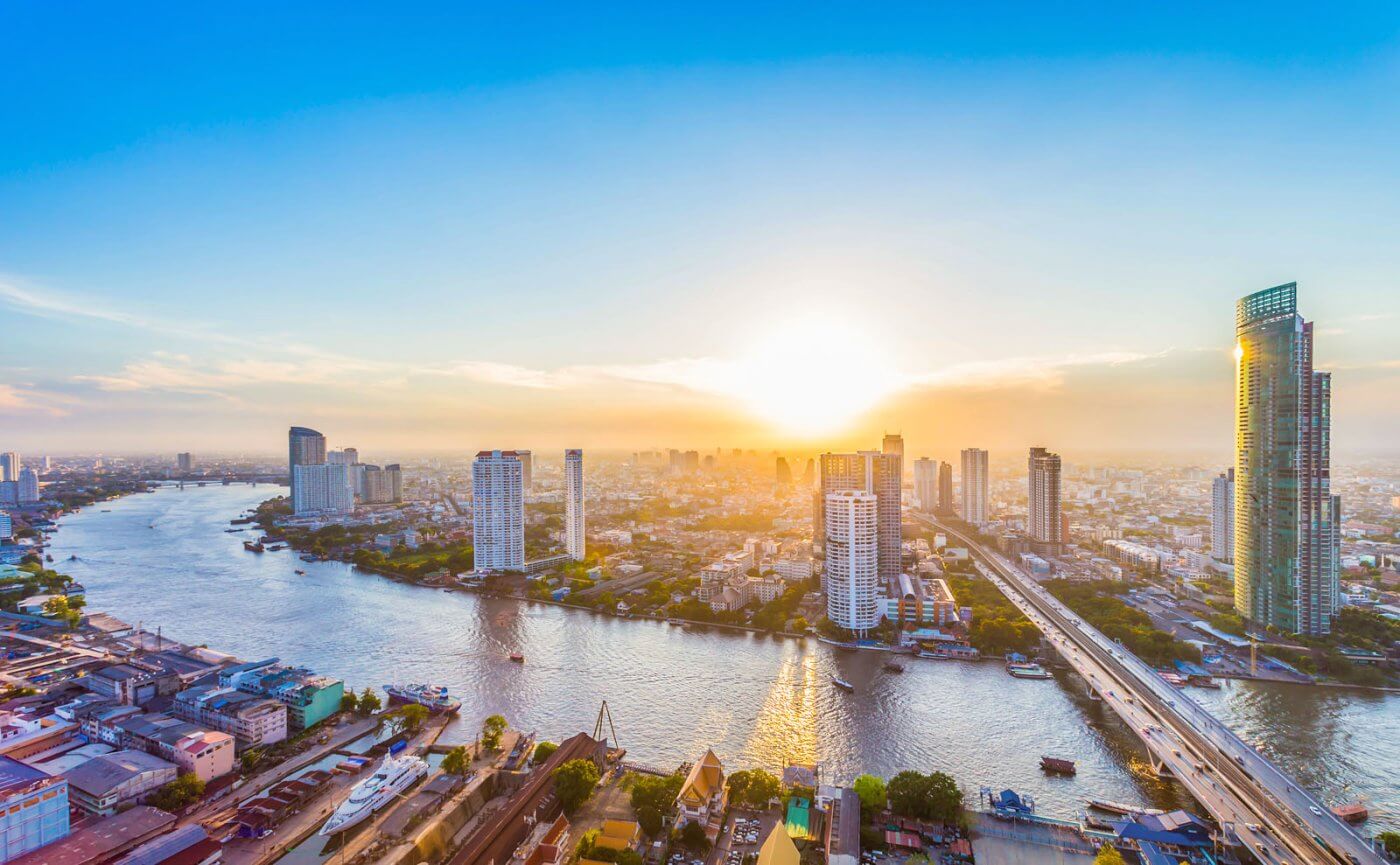 Stunning sunset over Bangkok's skyline, with the Chao Phraya River reflecting vibrant colors and modern skyscrapers.