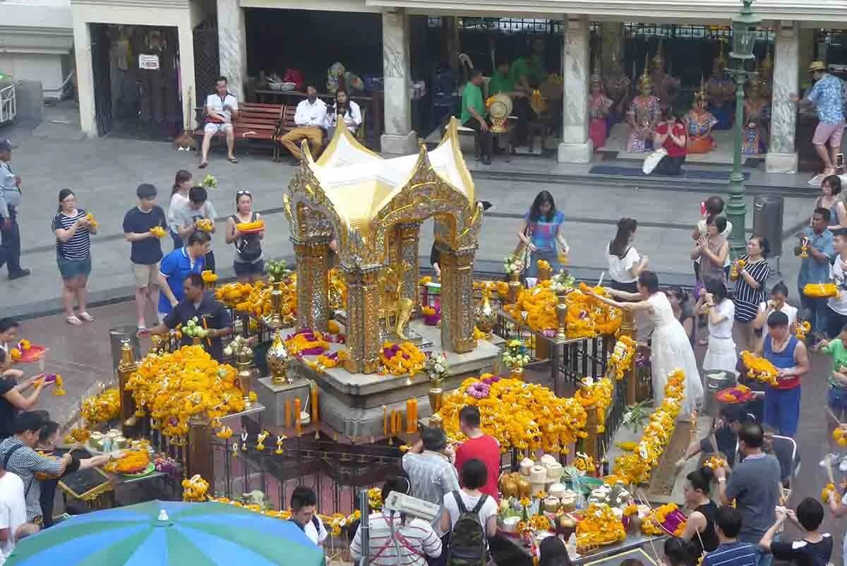 Devotees offering yellow flowers and fruits at a golden shrine, celebrating cultural and spiritual traditions in a vibrant setting.