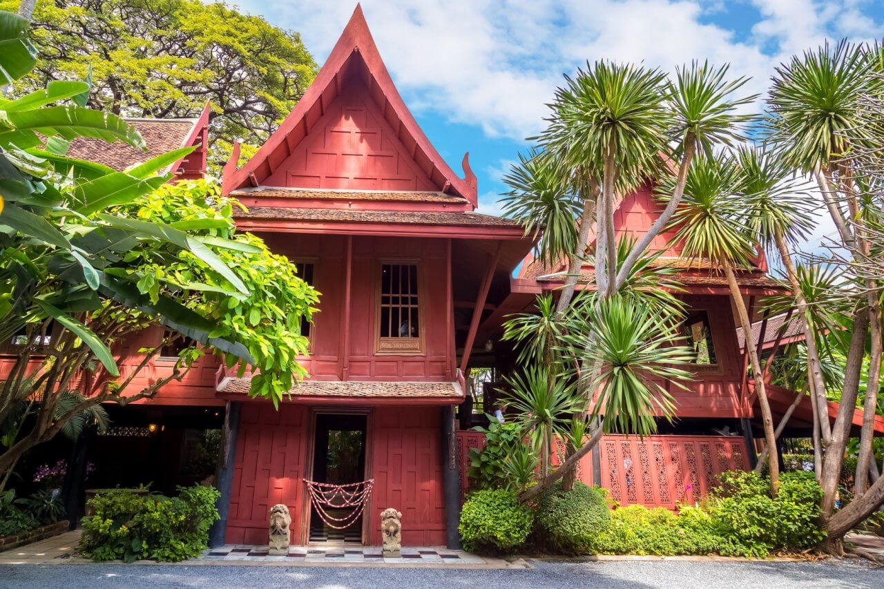 Traditional Thai-style architecture surrounded by lush greenery, featuring intricate wooden details and vibrant landscaping.