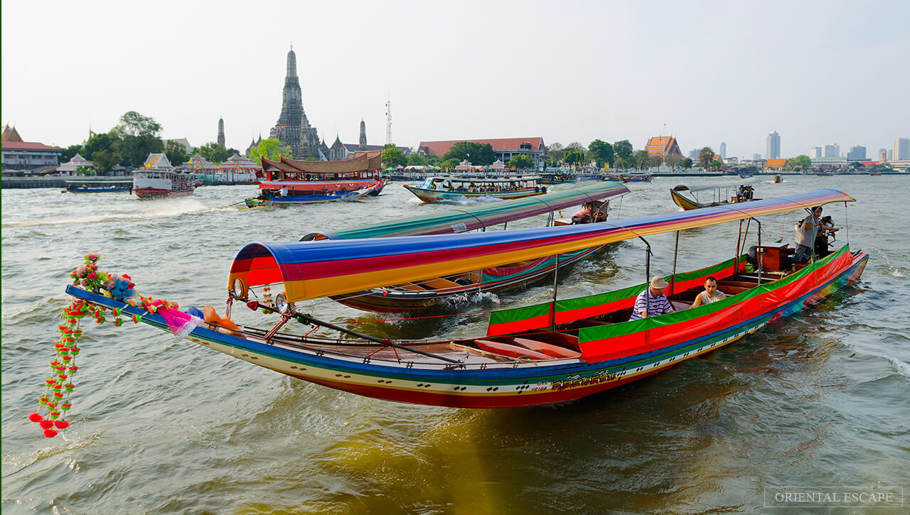 Colorful longtail boats navigate the bustling waters near the iconic Wat Arun temple in Bangkok, showcasing the city's vibrant culture.