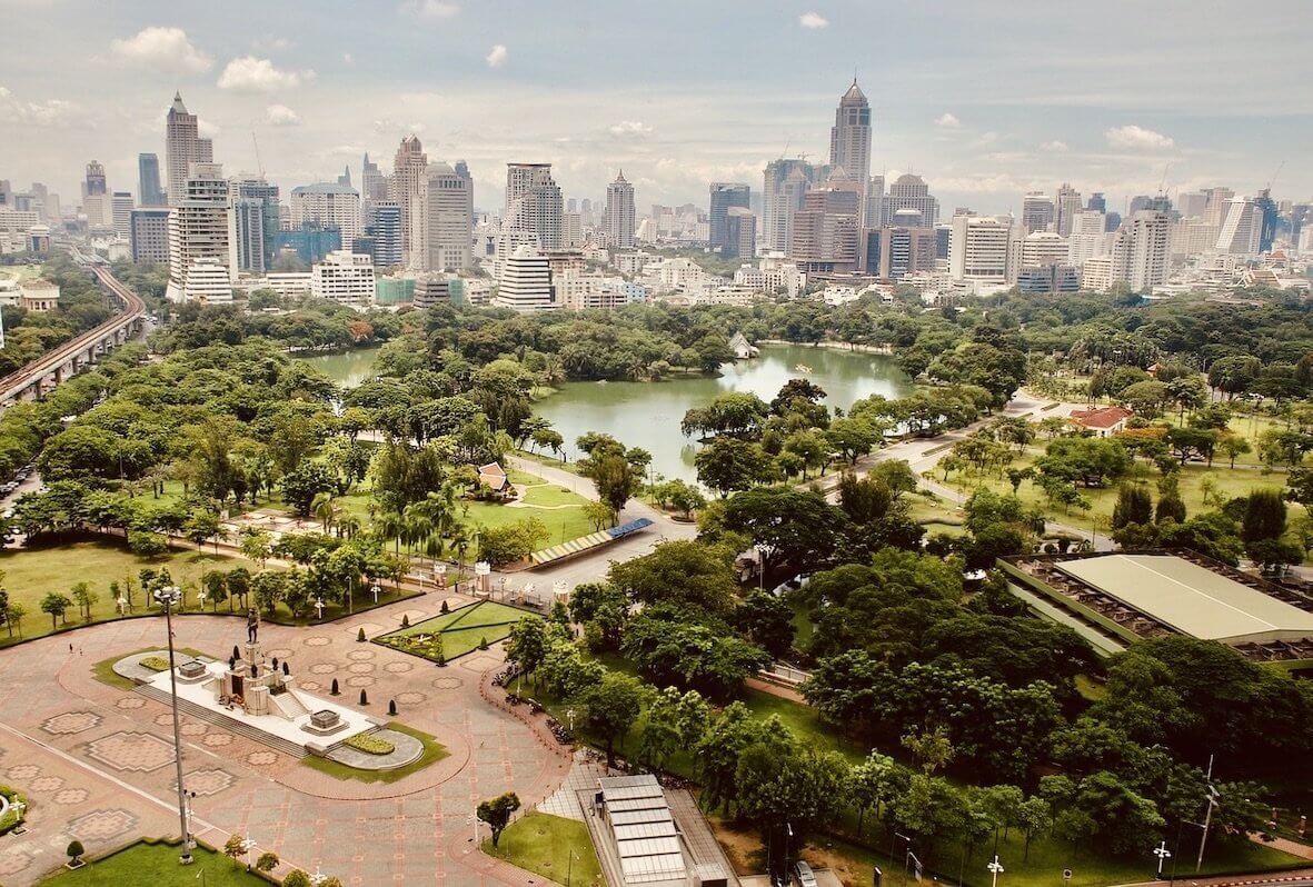 Lush urban park with a serene lake and towering city skyline, highlighting the blend of nature and modern living.