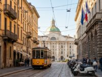 Charming Milan street with a vintage tram passing by stylish cafes and elegant architecture under a clear blue sky.