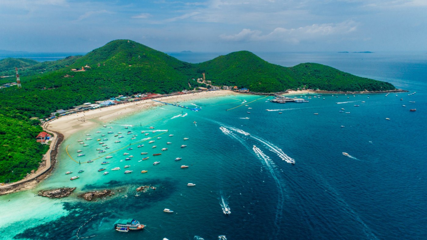 Aerial view of a vibrant tropical Pattaya beach in Thailand with boats, clear turquoise waters, and lush hills, perfect for vacation getaways.