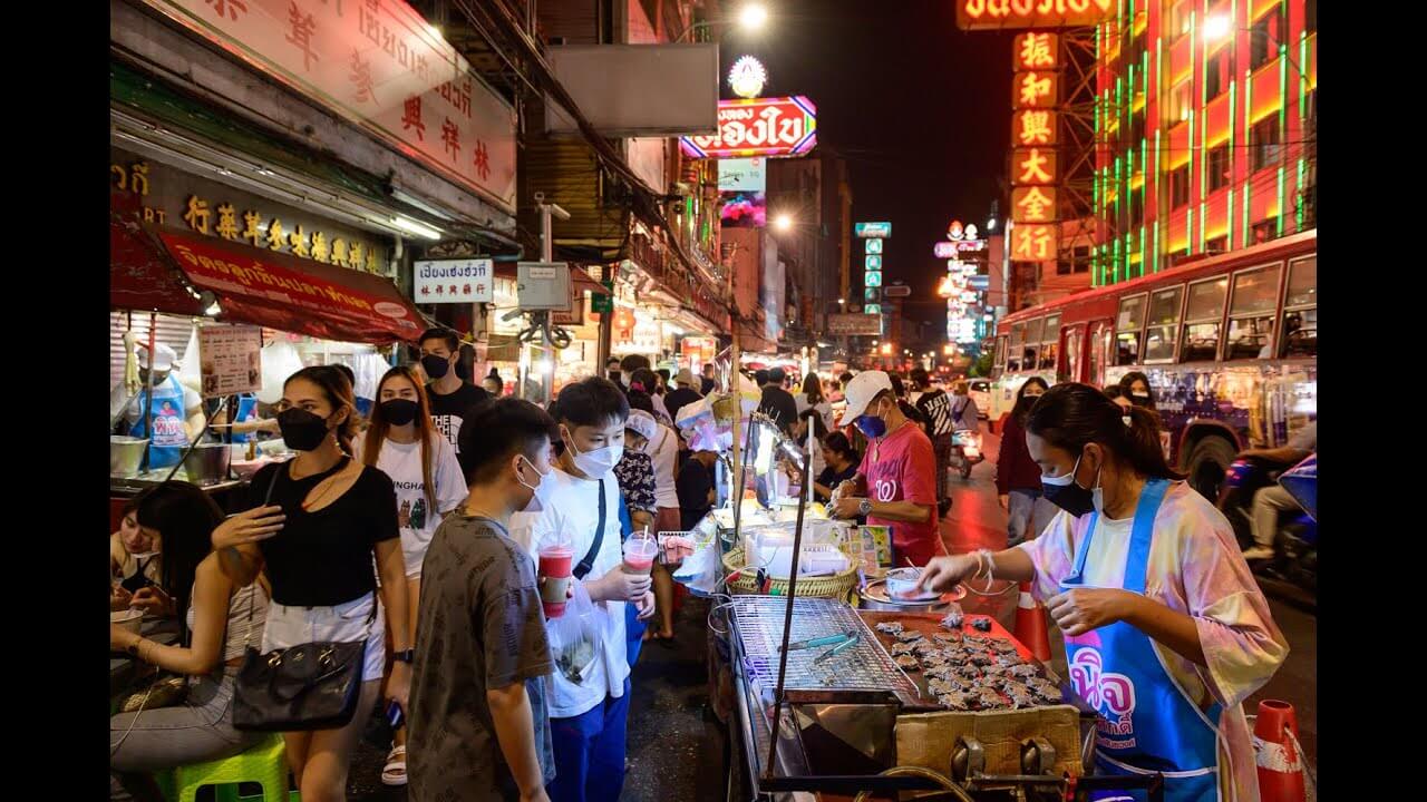 Bustling night market in Thailand, filled with people enjoying street food and vibrant neon signs illuminating the scene.