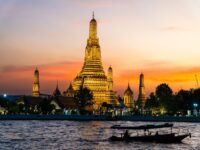 Wat Arun illuminated at sunset with boats on the Chao Phraya River, showcasing Bangkok's stunning skyline and rich culture.